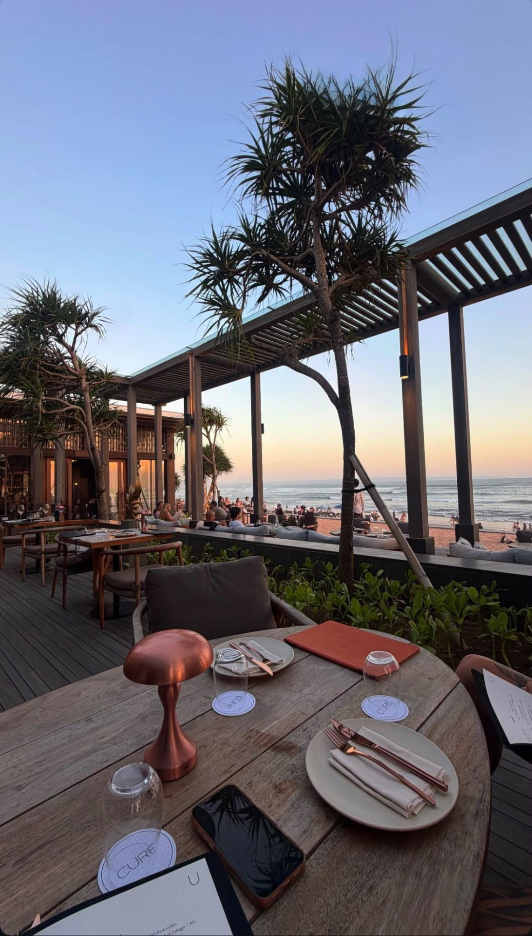 An elegantly set seaside dining terrace framed by palms at sunset