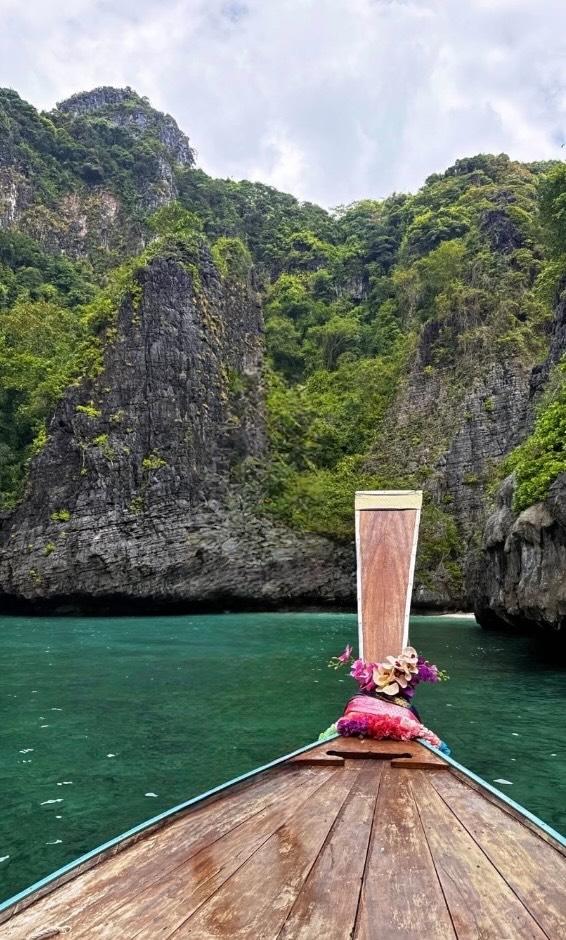 The flower-decked bow of a wooden long-tail boat gliding through a turquoise lagoon