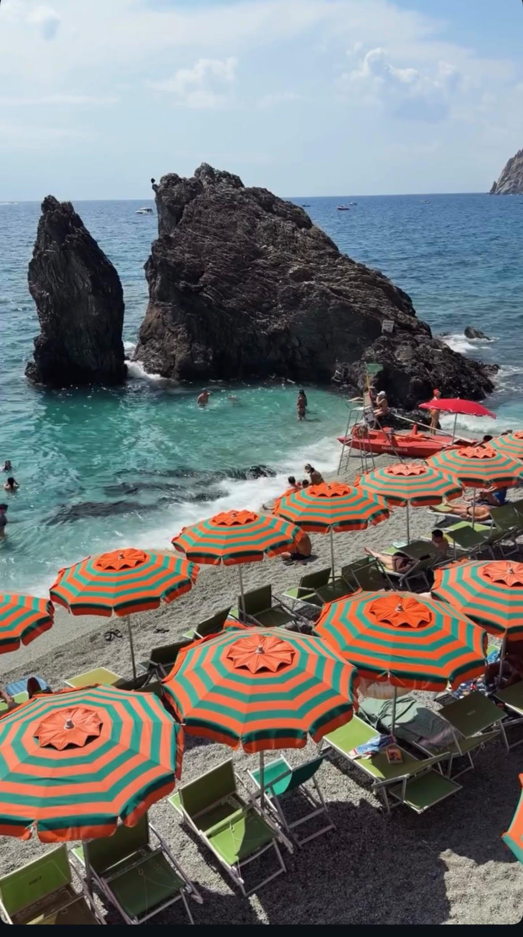 Colorful striped beach umbrellas beside turquoise water and coastal rock formations