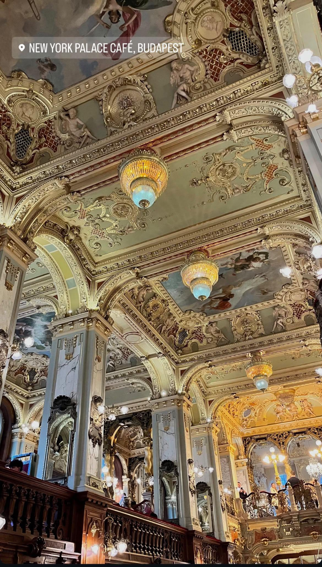 An ornate cafe interior with gilded ceilings, chandeliers and decorative columns