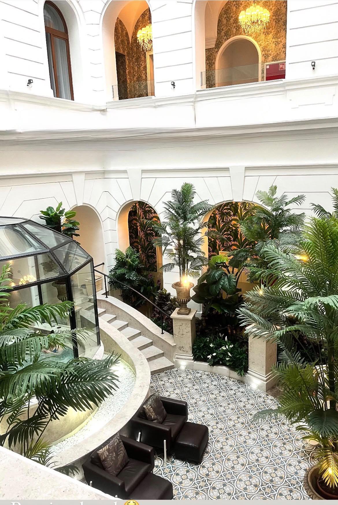 A light-filled hotel atrium with elegant arches, palms and a sweeping staircase