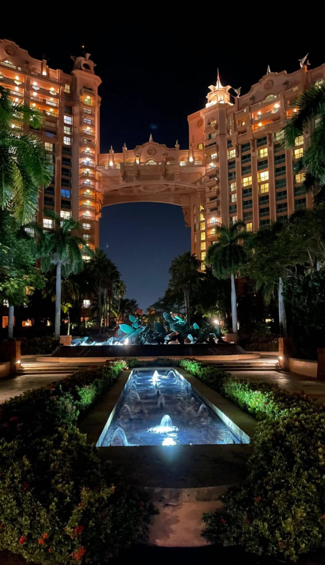 An illuminated grand resort and reflecting fountains at night